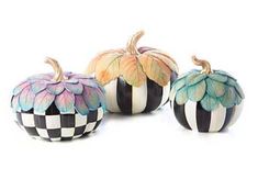 three painted pumpkins sitting next to each other on a white surface with black and white checkerboard