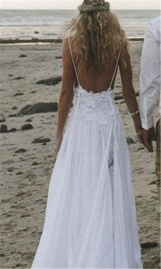 a woman in a white dress walking on the beach with her back to the camera