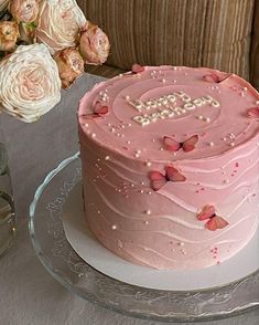 a pink frosted cake sitting on top of a glass plate next to flowers and a vase