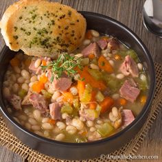 a bowl of soup with ham, beans and carrots next to a piece of bread