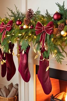 stockings hanging from a mantel decorated with pine cones and red ribbon, christmas decorations