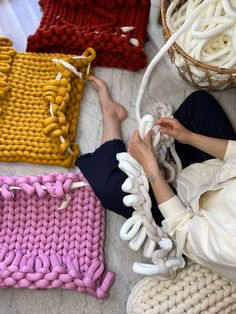 a woman sitting on the floor next to several knitted items in different colors and sizes