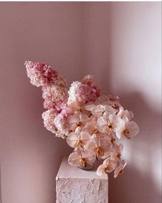 a vase filled with pink and white flowers on top of a wooden table next to a wall