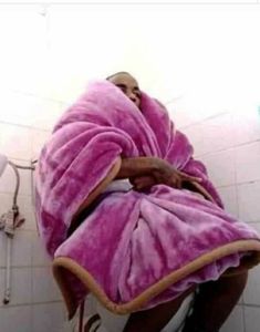 a man wrapped in a pink towel sitting on top of a toilet