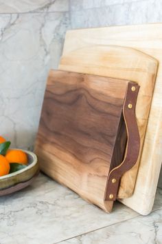 a wooden cutting board sitting on top of a counter next to an oranges bowl