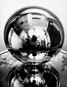 the reflection of two people standing in front of a metal ball on top of a table