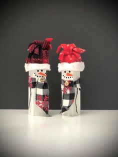 two snowmen wearing hats and scarfs sitting in tin canisters with ribbons