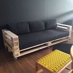 a couch made out of wooden pallets in a room with black walls and wood flooring