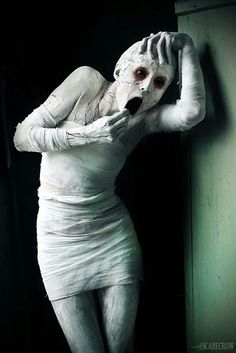 a woman dressed as a ghost with her hands on her head, leaning against a wall