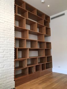 an empty bookcase in the corner of a room with white brick wall and hardwood flooring