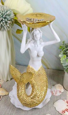 a white and gold statue holding a tray on top of it's head in the shape of a mermaid