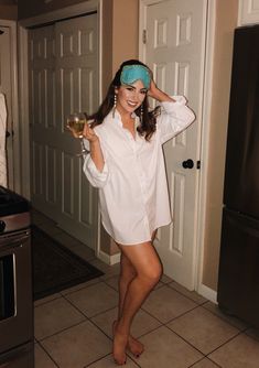 a woman standing in a kitchen holding a glass of wine and wearing a headband