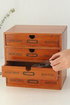 a person holding scissors in front of three drawers that are labeled with different types of buttons