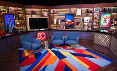 a brightly colored room with two blue chairs and a colorful rug on the floor in front of it