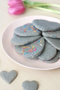 some heart shaped cookies on a plate with sprinkles and pink tulips in the background