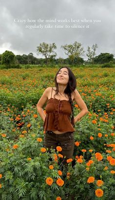 a woman standing in a field full of flowers with her hands on her hips looking up at the sky