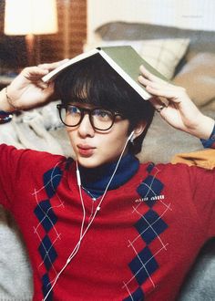 a young man wearing glasses and holding a book over his head while sitting on a couch