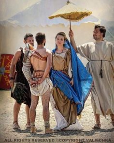 three people dressed in roman clothing and holding an umbrella