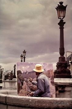 a man sitting on a bench next to a lamp post with a painting in front of him