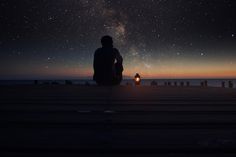 a person sitting on a dock looking at the night sky