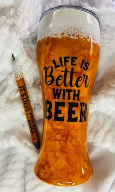 a beer glass with the words life is better with beer written on it next to a pen