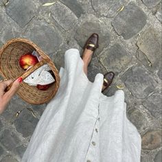 a person sitting on the ground with an apple in a basket next to their feet