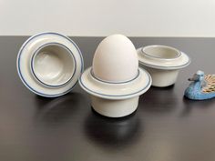 an egg sitting on top of two white bowls next to a blue bird figurine