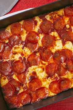 a pepperoni pizza in a pan on a red table