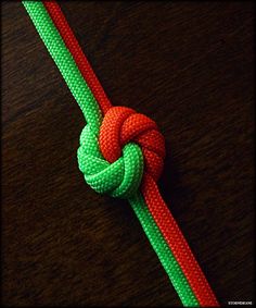 a red and green rope with a knot on it sitting on top of a wooden table