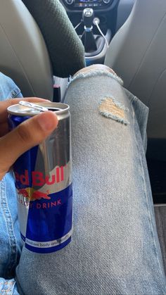 a can of red bull drink sitting on someone's lap in the back seat of a car