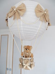 a teddy bear in a hot air balloon with bows on it's head is suspended from the ceiling