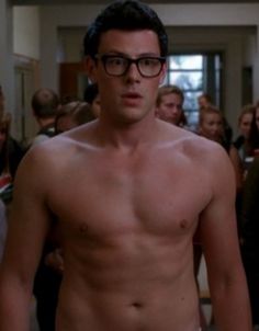 a shirtless man with glasses standing in front of a group of people