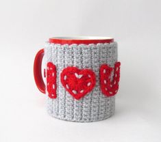 a crocheted coffee cup with red hearts on the inside and bottom, sitting on a white surface