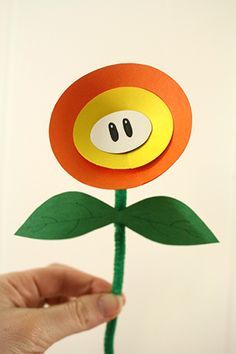 a hand holding up a paper flower with a smiley face on it