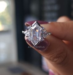 a woman's hand holding an engagement ring in front of her face with the center stone surrounded by diamonds