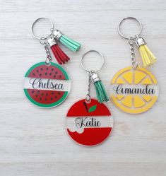 three personalized key chains with fruit and tassels on them sitting on a table