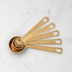 six gold measuring spoons with engraved names on them sitting on a white marble surface