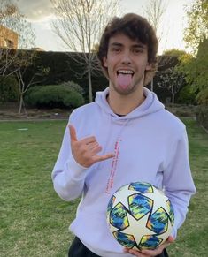 a young man holding a soccer ball and making a funny face with his tongue out