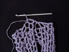 a crocheted piece of cloth next to a knitting needle on a black surface