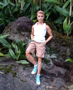 a young man standing on top of a rock in front of some plants and rocks