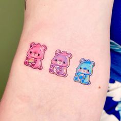 three small tattoos on the arm of a woman's left arm, each with different colored teddy bears