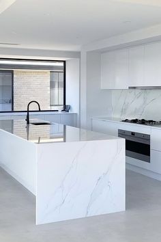 a white kitchen with marble counter tops and an island in front of the stove top