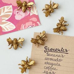 three gold bee pins sitting on top of a piece of paper next to a note