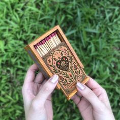 a person holding up a match box with matches in it on top of some grass