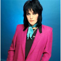 a woman with black hair wearing a pink jacket and blue scarf around her neck is posing for a photo