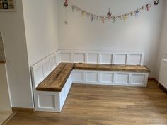 an empty room with white walls and wooden bench in the corner, decorated with christmas lights