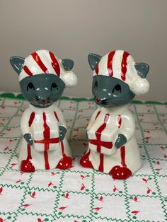 two ceramic figurines sitting on top of a table covered in red and white decorations