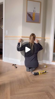 a woman sitting on the floor in front of a wall with paint and tools around her