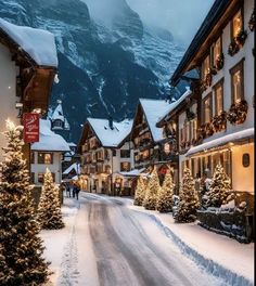 a snowy street with christmas trees and lights on the sidewalks in front of buildings that have snow covered mountains behind them