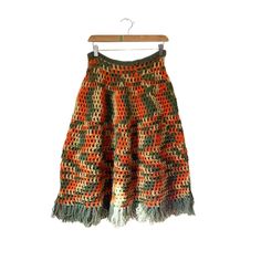 a crocheted skirt hanging on a wooden hanger with an orange and green pattern